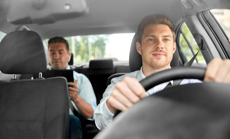 A man driving a car with a passenger in the backseat