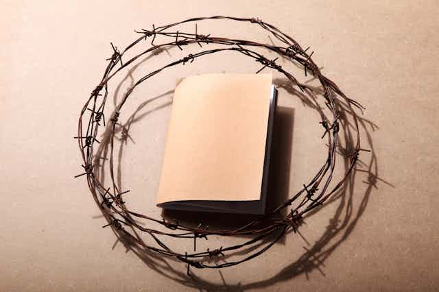 A beige book is surrounded by barbed wire.