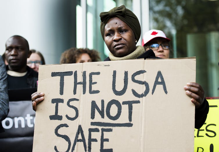 A Black woman in tears holds a sign that says The USA is Not Safe.