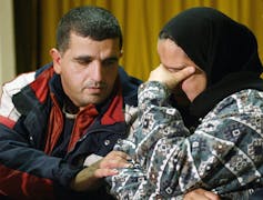 A man comforts a woman, who has her hand on her face as she cries.