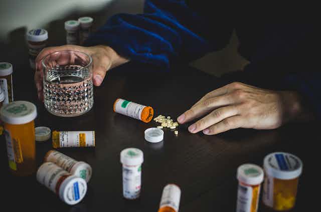 Hands surrounded by pill bottles on a table