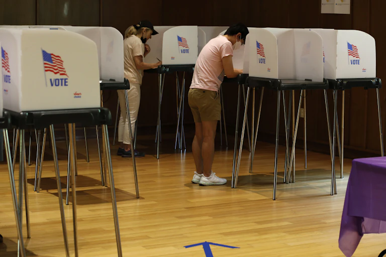 People standing at voting stations in a large room.
