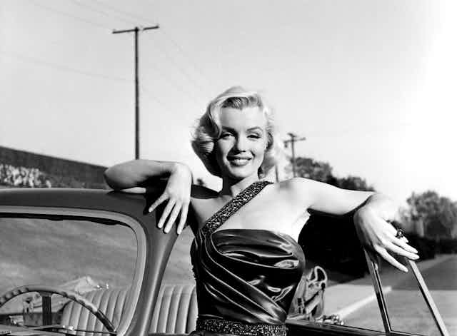 Marilyn Monroe leaning on an open-top car.
