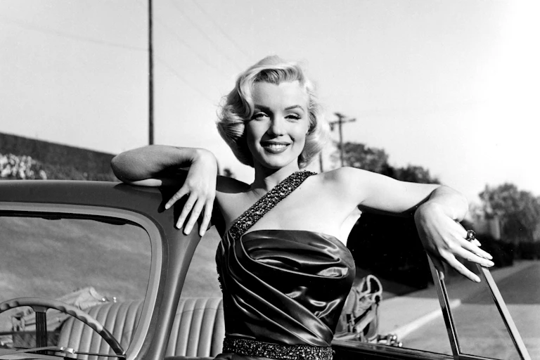Marilyn Monroe leaning on an open-top car.