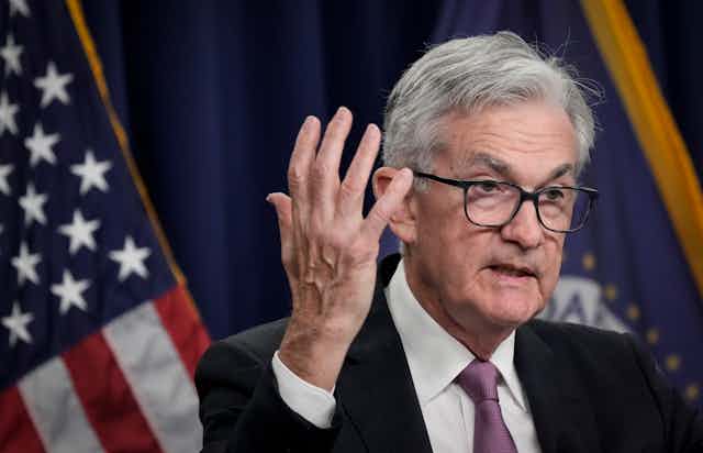 Fed Chairman Jerome Powell wearing glasses and in a grey suit gesticulates to the camera.