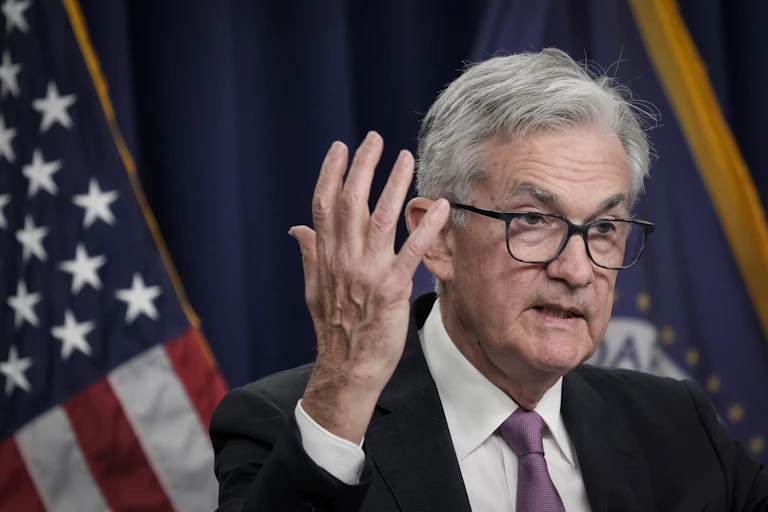 Fed Chairman Jerome Powell wearing glasses and in a grey suit gesticulates to the camera.