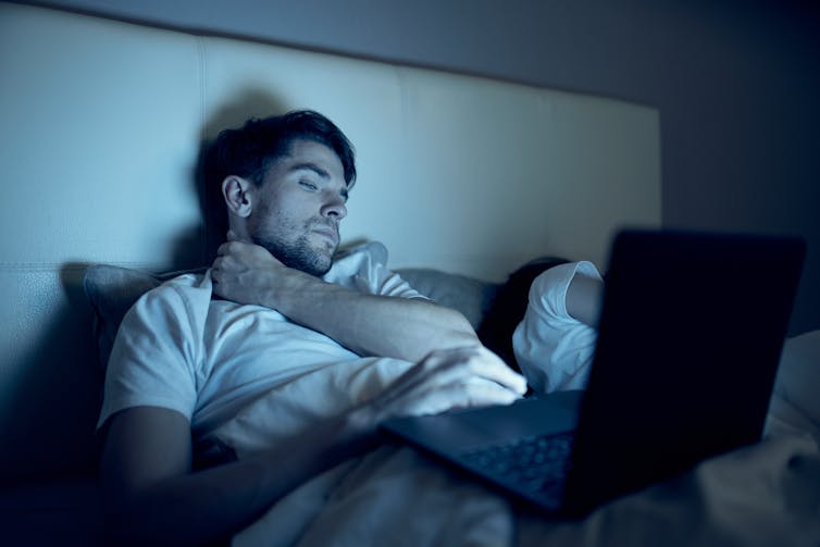 A man lying on his bed and looking at his computer.