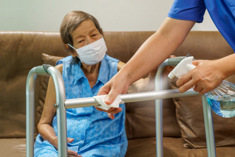 Frail elderly person sits on a couch while an aged care worker cleans her frame