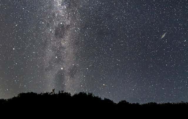 Photo of a starry night sky, flanked with a silhouette of trees at the bottom