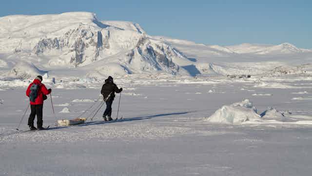 Two expeditioners walk across the snow in Antarctica
