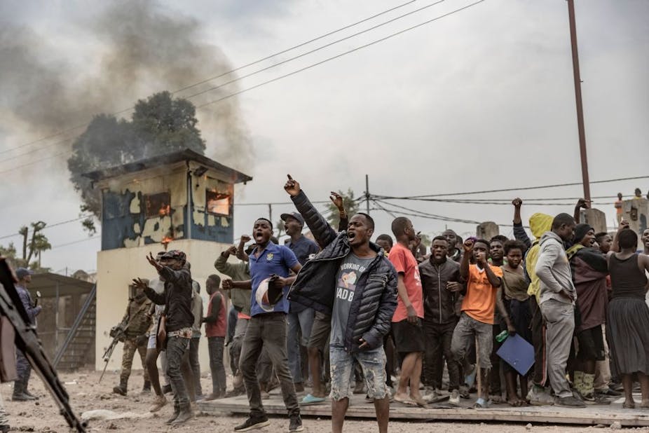 Men raising their fists in protest in front of a burning building.