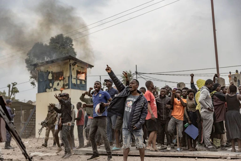 Men raising their fists in protest in front of a burning building.