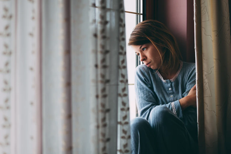 A sad young woman looks out of a window.