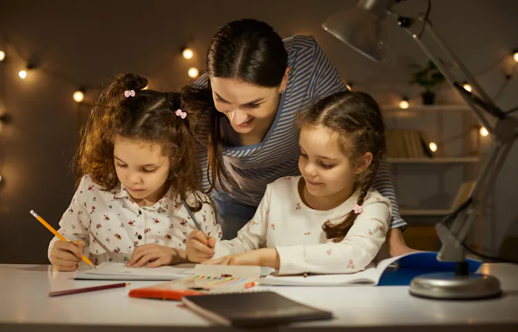 Une mère affectueuse regardant des enfants d’âge préscolaire dessiner et écrire