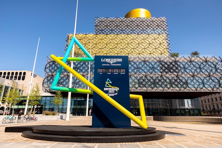A clock in front of a library under a blue sky.