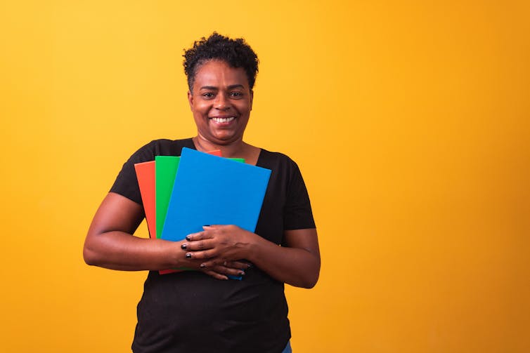 A person is smiling and holding binders.