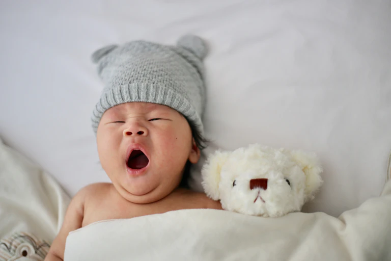 Un nourrisson couché dans son lit, avec un toutou ourson, en train de bailler