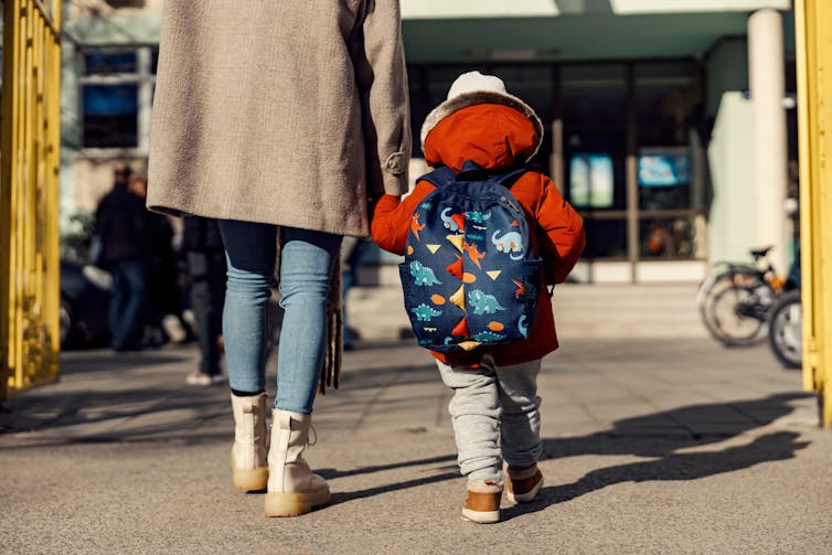The back of a child and adult seen holding hands.