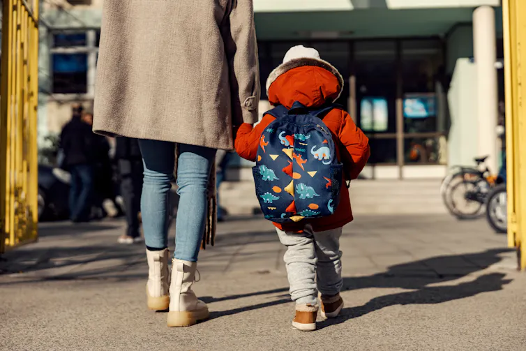 The back of a child and adult seen holding hands.