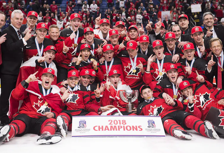 Players and coaches are grouped together on the ice with a sign that says 2018 champions.