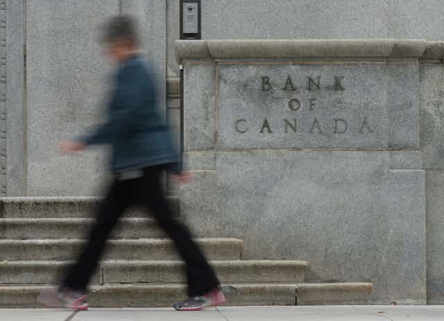 A blurry figure walks past the Bank of Canada building sign in Ottawa