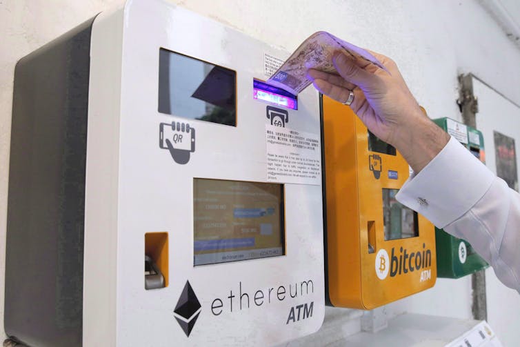 A man puts a paper bill in an ATM that says 'ethereum' across the front
