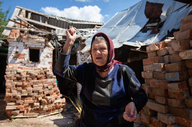 A Ukrainian woman shakes her fist, standing outside her detroyed home in Makariv, near Kyiv.