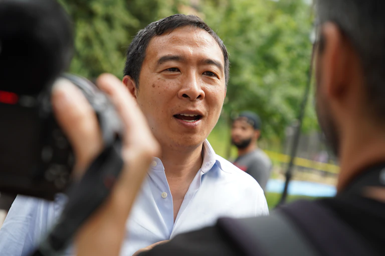 A man with short dark hair being filmed while talking to someone.