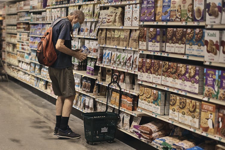 a man looks at two boxes of breakfast food in front of an aisle of cereals and other foods