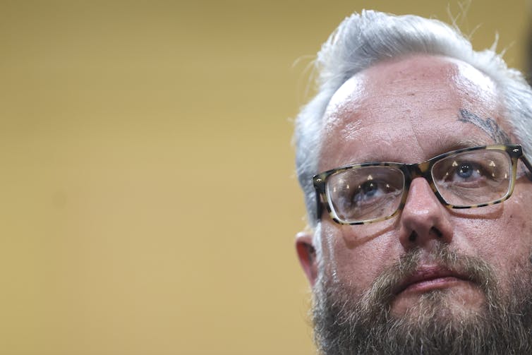 A middle-aged white man with gray hair and brown beard answers questions from a congressional committee.