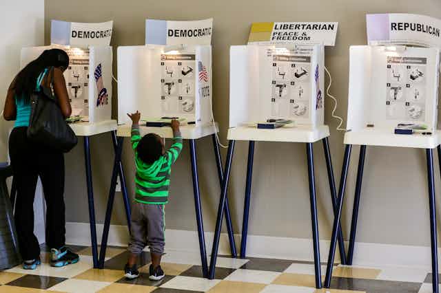 A Black mother going over ballot as her son explores the booth next to hers