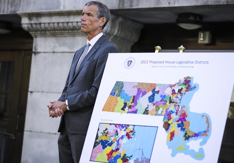 Lawmaker stands next to map of Massachusetts state legislative districts