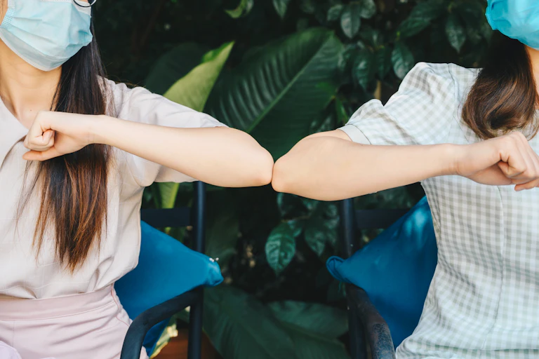 Two masked women doing an elbow greeting