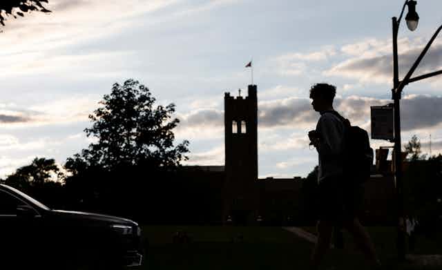 A silhouetted student is seen walking at dusk on a campus.