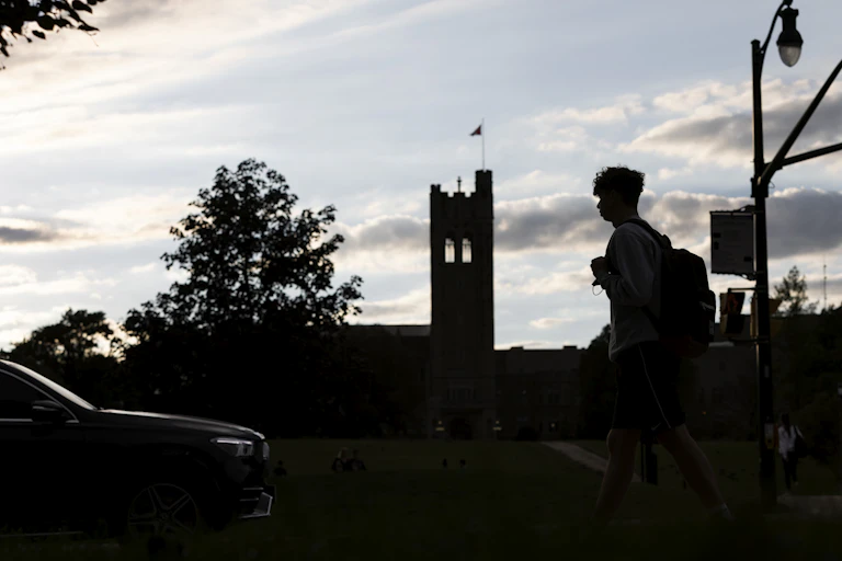 A silhouetted student is seen walking at dusk on a campus.