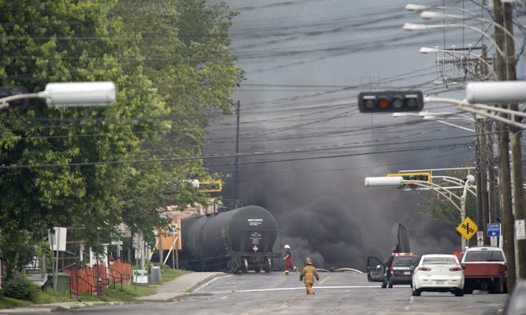 A street scene with billowing smoke in the background and a firefighter in the foreground