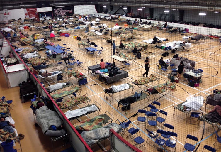 A gymnasium filled with cots and folding chairs