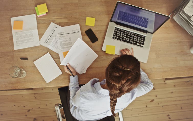 A woman working at a desk with papers and a laptop.