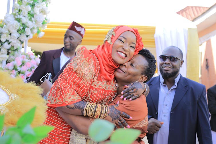 A bride in orange hugs her mother.