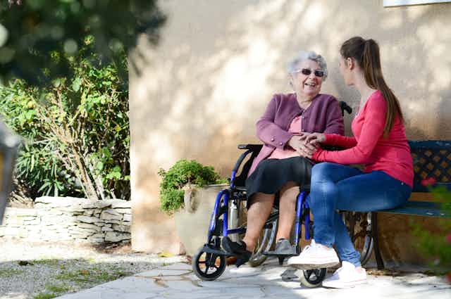 A woman in a wheelchair outside engaging happily with a younger woman.