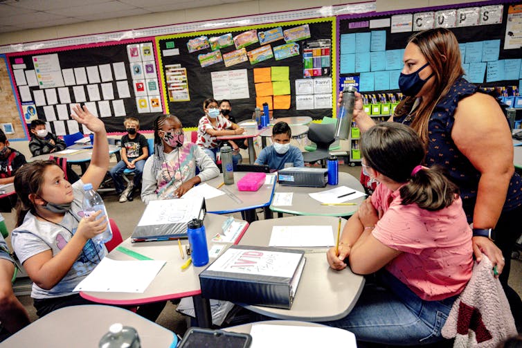 An adult stands in a classroom with several children sitting at desks