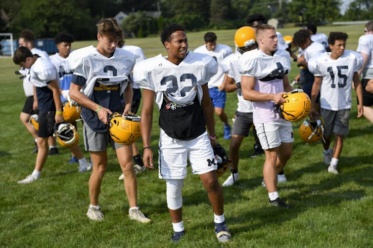 High school football players in shorts and minimal pads at a summer practice.