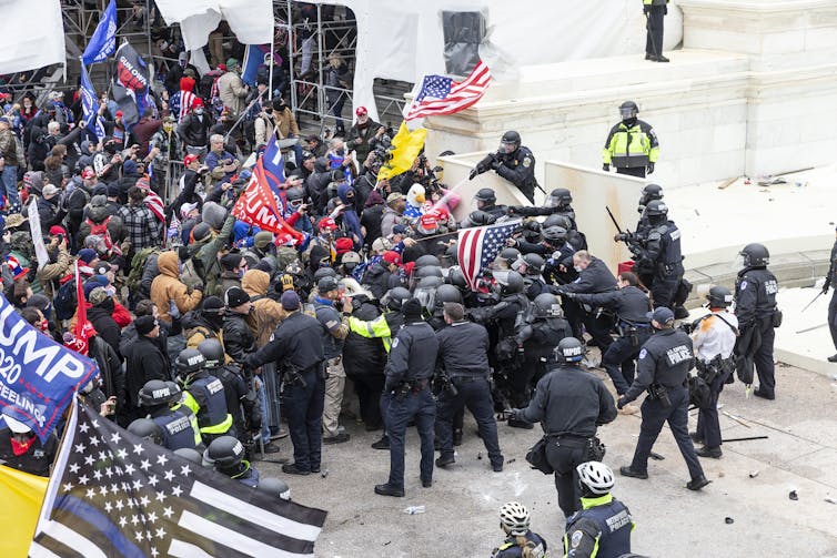 Protesters waving Trump flags storm the U.S. Capitol while police officers try to hold them back.