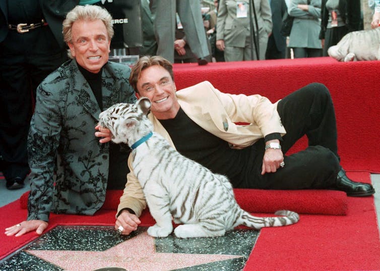 Dua pria berjas berpose dengan seorang bintang di karpet merah Hollywood Walk of Fame dengan kapal selam harimau putih