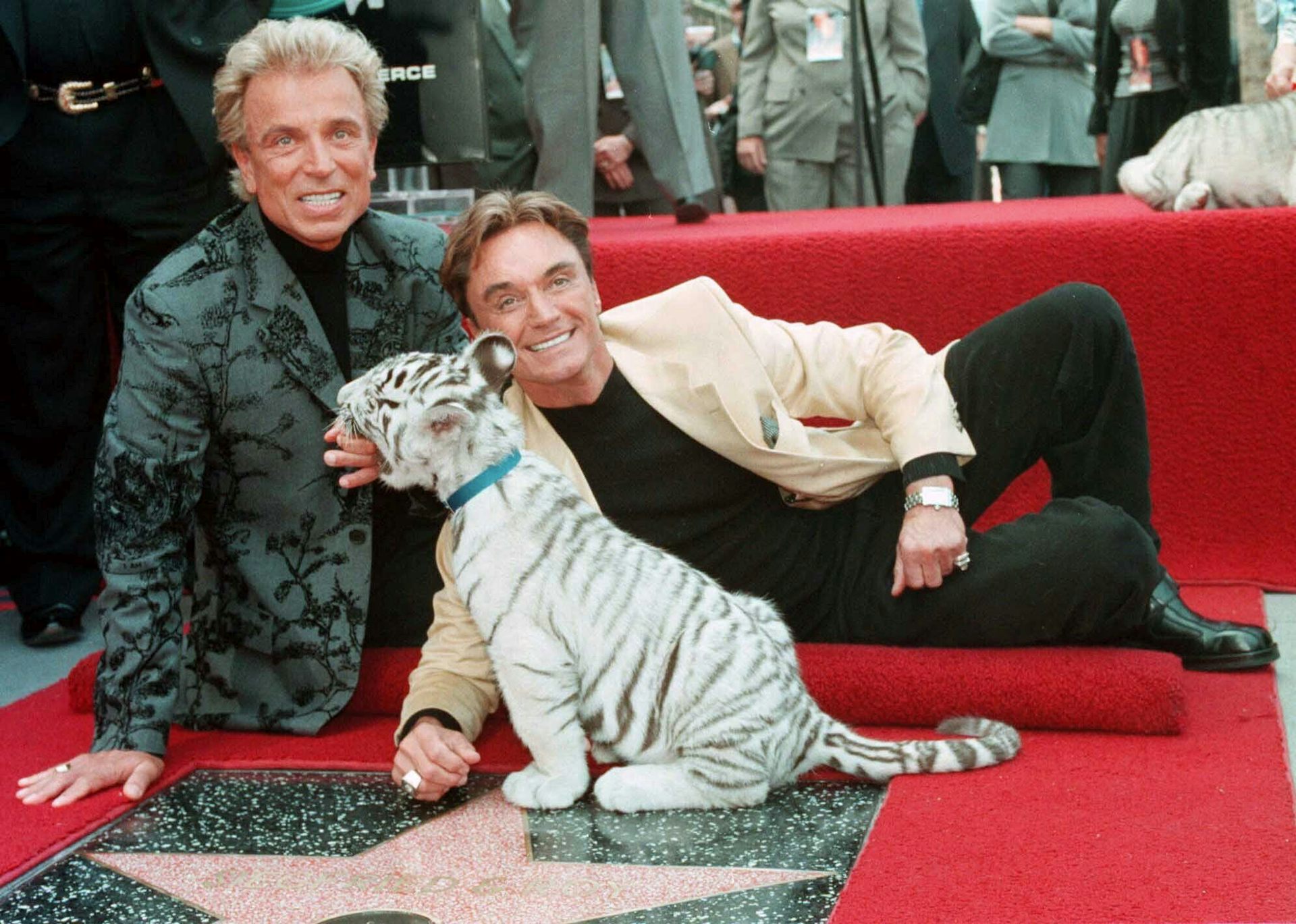 Two men in suits pose with a star on the Hollywood Walk of Fame red carpet with a white tiger sub