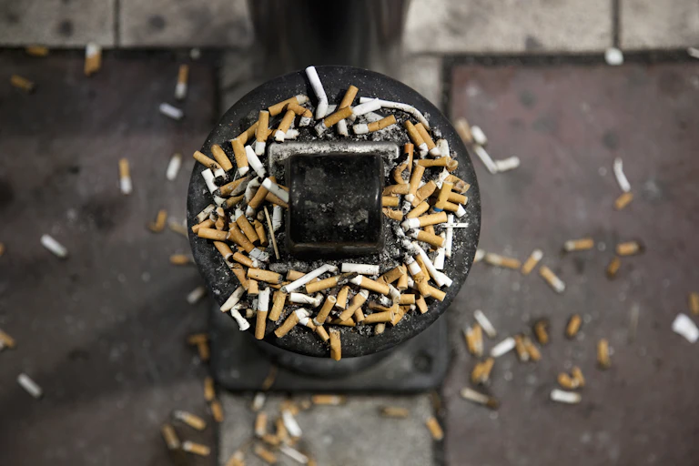 Cigarette butts spilling out of an outdoor ashtray and onto the ground around it.