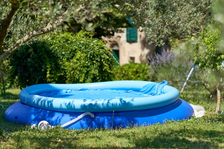 A blue, plastic paddling pool in a garden with a white filter attached.