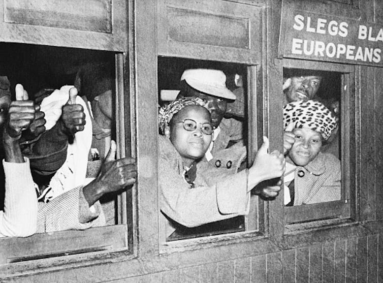Men and women give the thumbs up sign from inside a train coach reserved for whites only in 1952, during apartheid. A sign on the train says 'Europeans only'.