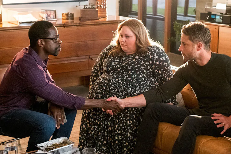 Dos hombres se dan la mano cerrando un trato mientras una mujer los observa en el centro.