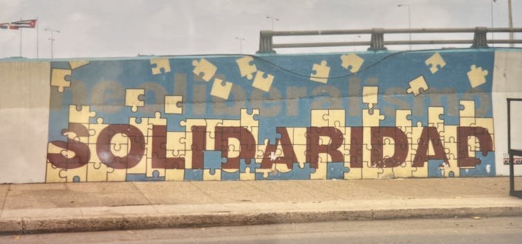 Mural with 'neoliberalismo' written in light-gray text and 'solidaridad' written below it in bigger, red text.